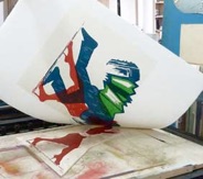 Foto: ein Holzschnitt wird gedruckt, die Farbe rot wird gerade abgezogen